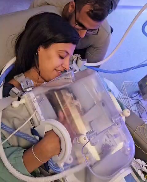 A mother holding her baby in the Skincubator, the father leaning in beside her