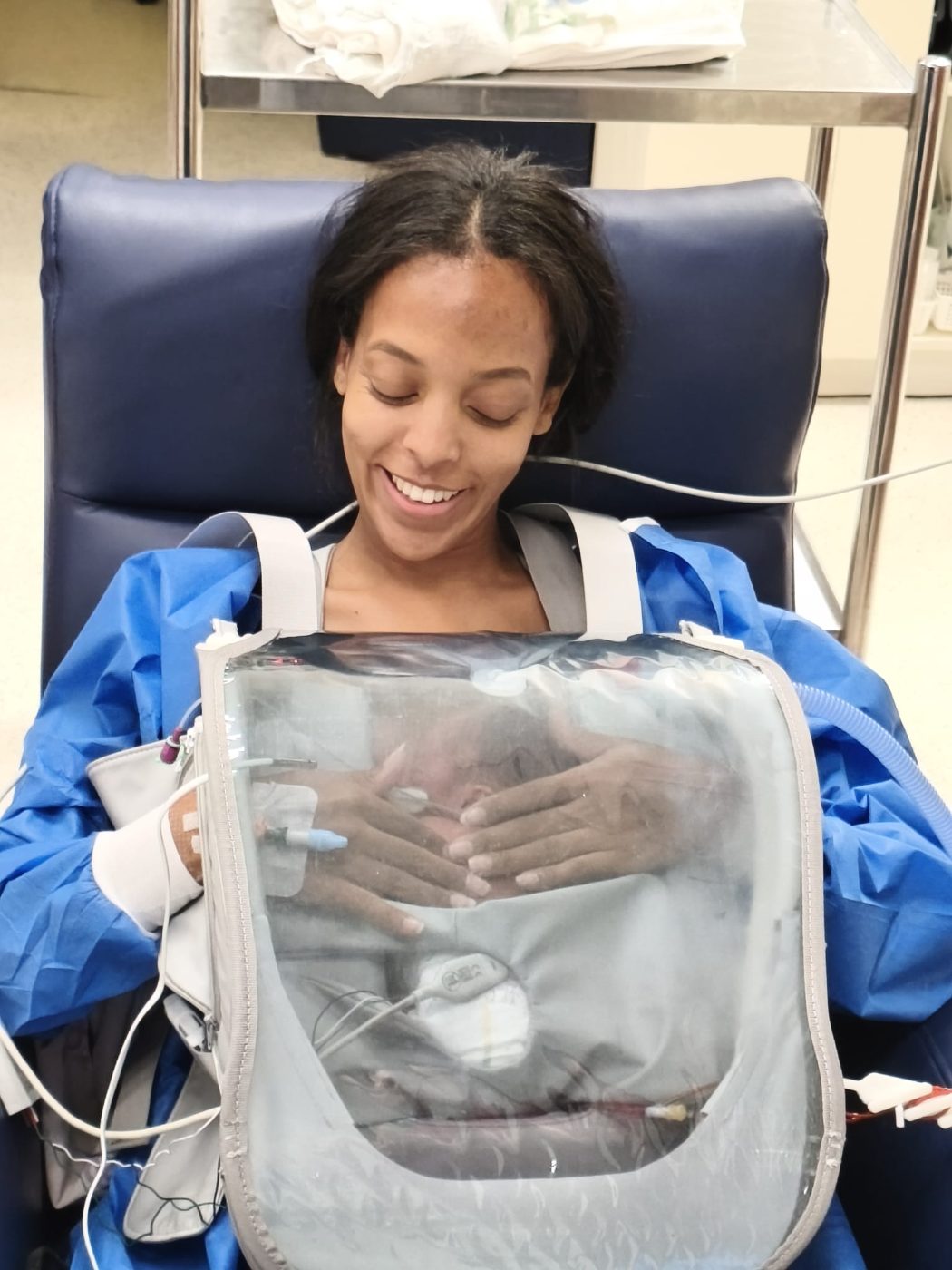 A mother smiling with both hands on her baby, held in the Skincubator through a long session