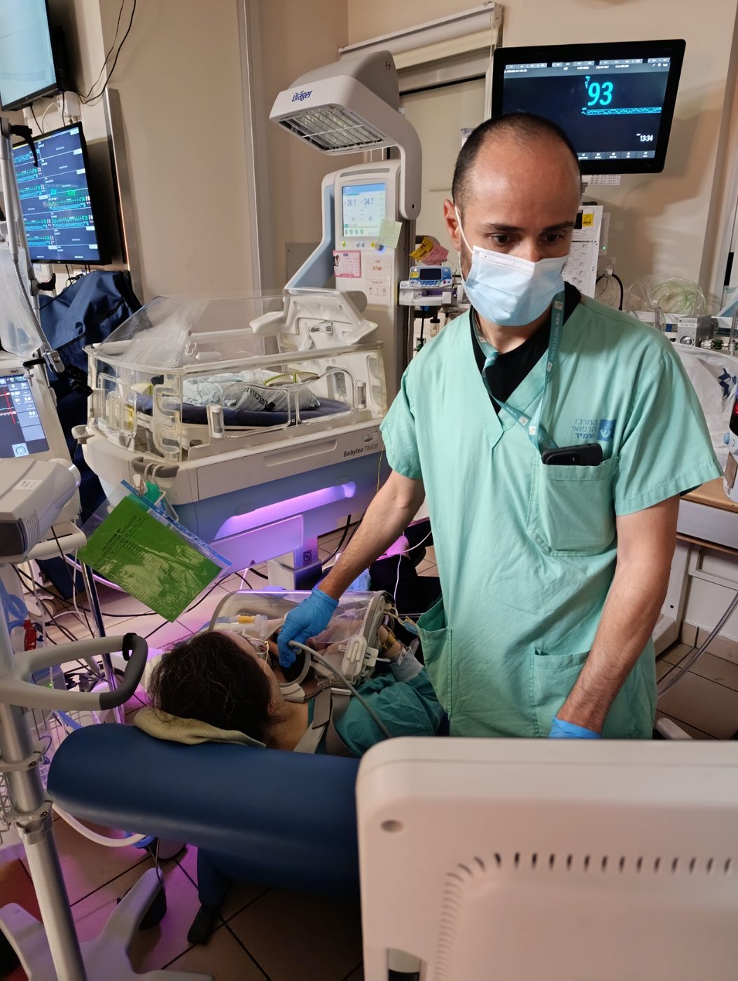 A clinician performing a procedure at the bedside while the baby stays held on a parent's chest
