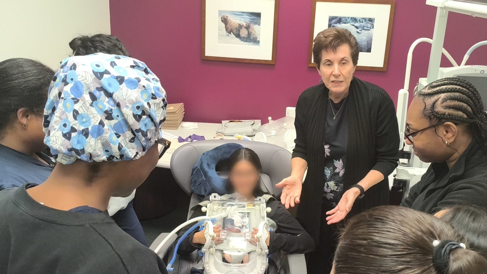 A NICU team gathered around a mother holding a manikin in the Skincubator, during a hands-on training session